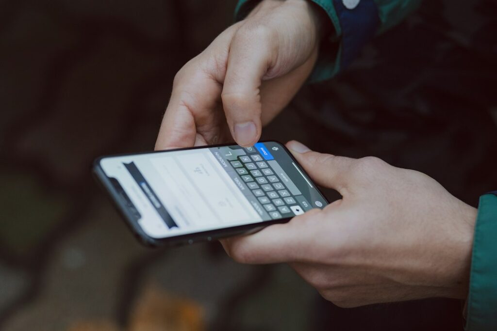 Close-up of two hands holding a smartphone and typing on its on-screen keyboard.